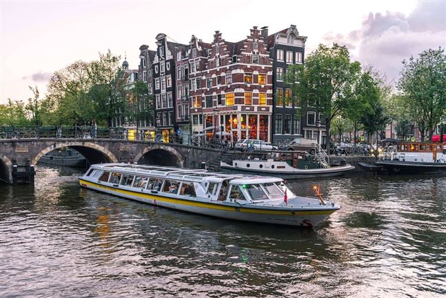 Crucero en barco por un típico canal de Ámsterdam rodeado de casas de comerciantes