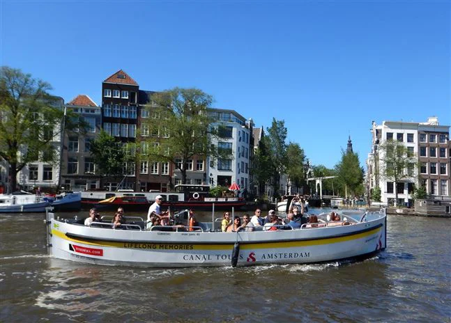Side view on open boat tour by Canal Tours Amsterdam in summer