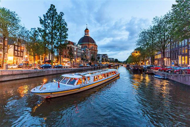Canal Tours Amsterdam boat cruising along a church at he canals during evening